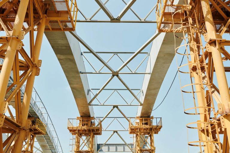 A striking low-angle view of a modern bridge under construction, highlighting beams and steel structures against a clear sky.