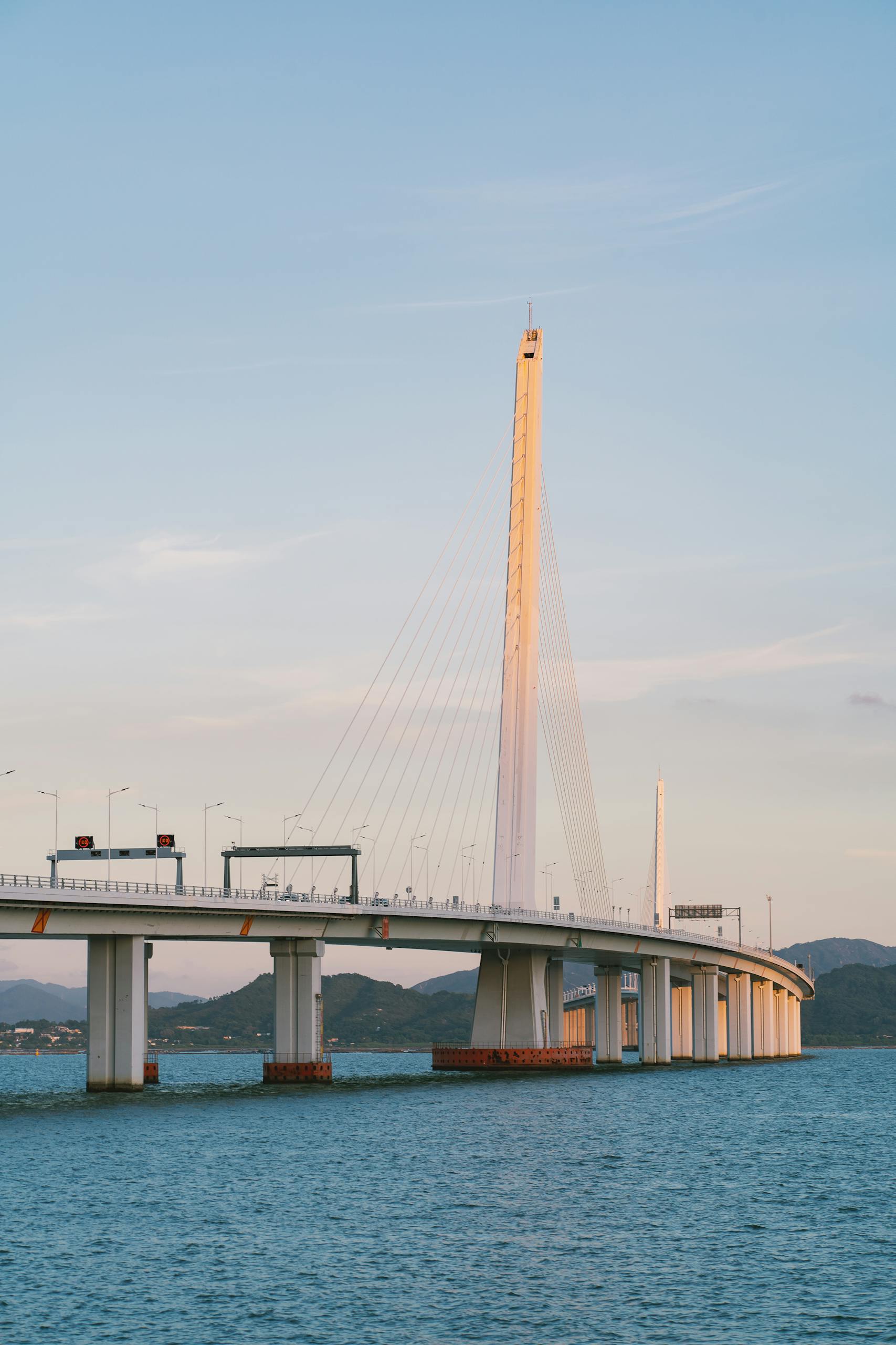 A captivating view of Shenzhen Bay Bridge arching over a serene sea, illuminated by sunset light.